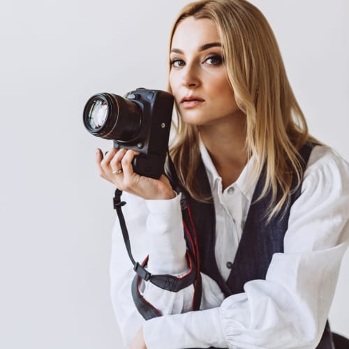 A beautiful woman photographer in a denim casual outfit and a white blouse with voluminous sleeves with a camera in her hands. Hobbies. Soft selective focus.